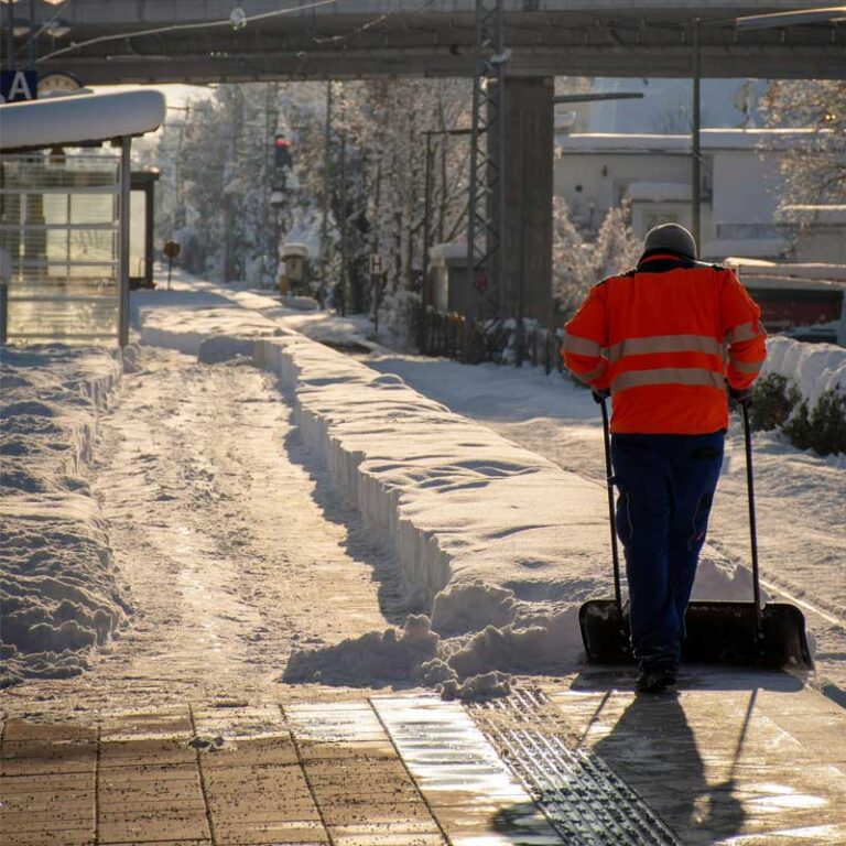 Person i reflexkläder som utför vägunderhåll genom att skotta en väg för hand under vintertid.