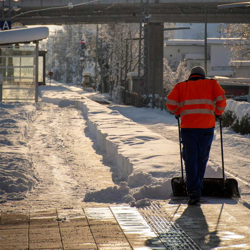 Person i reflexkläder som utför vägunderhåll genom att skotta en väg för hand under vintertid.