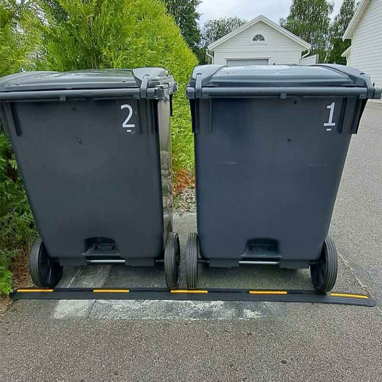 Två soptunnor står säkert bakom en låg list som hindrar dem från att rulla ut i gatan.