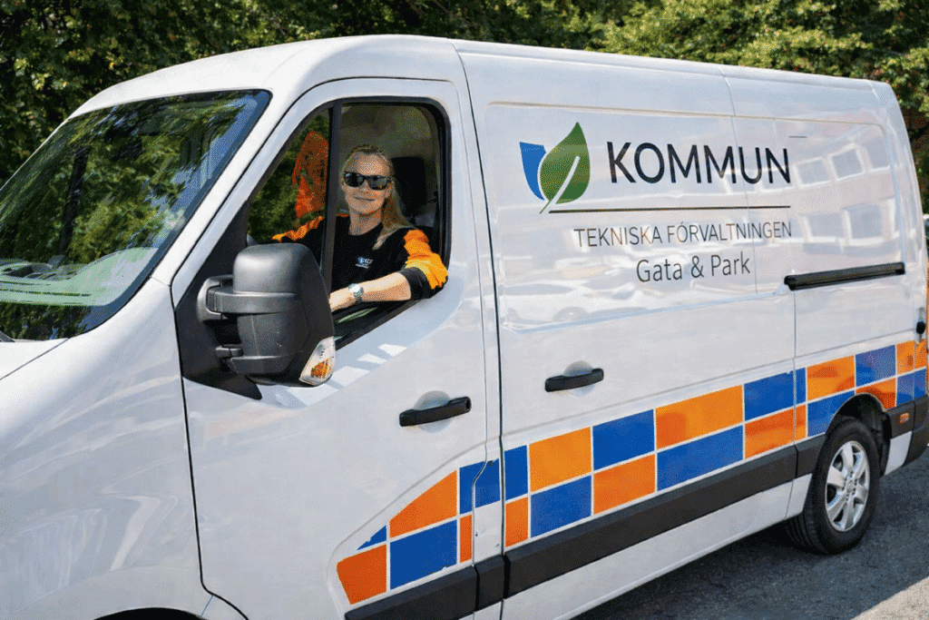 Kvinna från kommun tekniska förvaltning sitter i servicebil för gata och park, redo att arbeta med trafiksäkerhet och vägunderhåll i svensk miljö