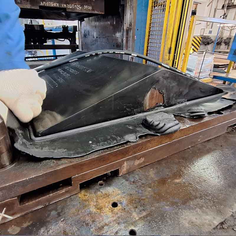 Operatör som lyfter en nytillverkad gummidetalj från formverktyget