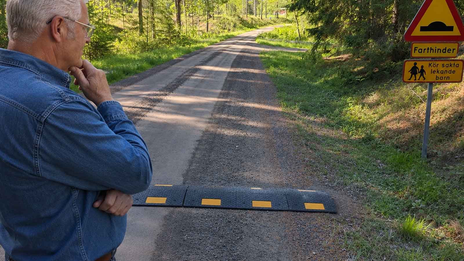Äldre man tittar på placering av farthinder på grusväg med varningsskylt för lekande barn i svenskt villaområde