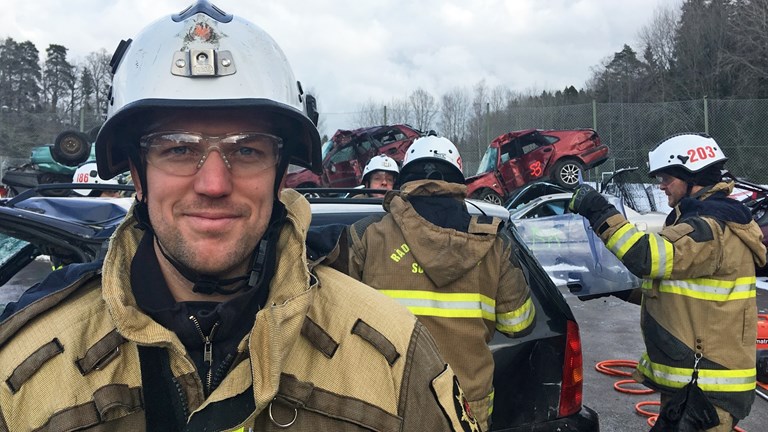 Tommy Carnebo i brandmansutrustning framför kollegor som arbetar med räddningsövning vid krockade bilar.