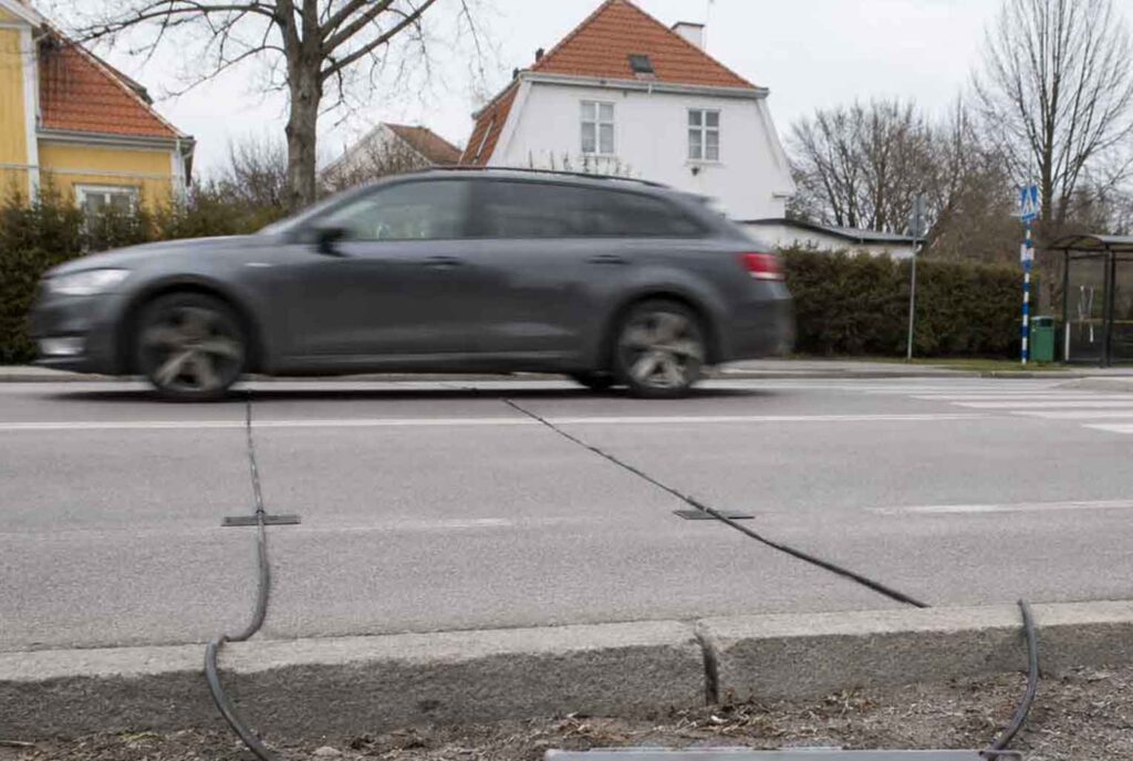 Trafikanalys med slangmätning i svenskt bostadsområde där en grå kombibil passerar över trafikanalys-slangar för mätning av hastighet och trafikflöde.