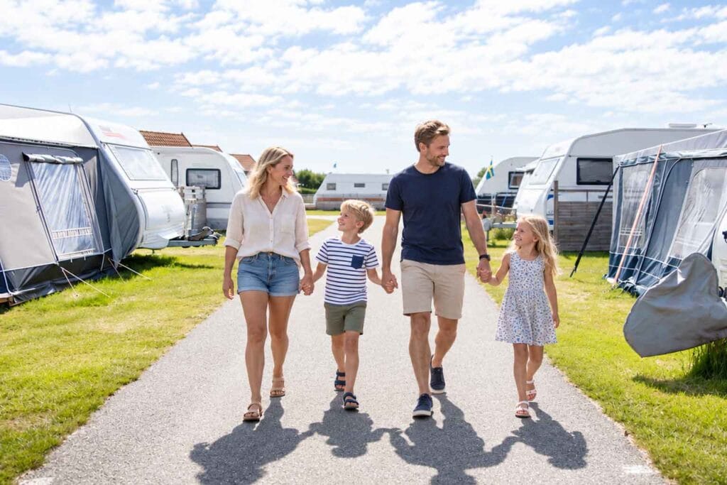 Familj med två barn går längs en väg mellan husvagnar på en svensk campingplats.