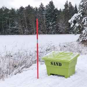 Grön sandlåda och rödvit snökäpp i snötäckt vintermiljö vid skogskant.
